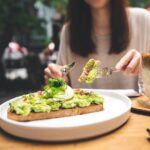 Tips for Weight Loss Without Exercise woman-cutting-avocado-toast-outdoor-restaurant